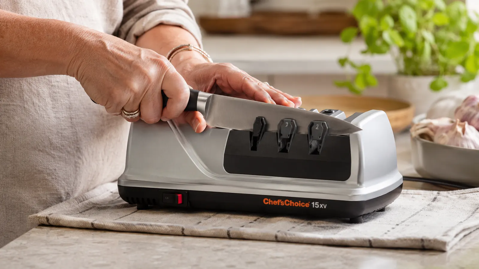 Hand drawing a chef's knife through the Chef'sChoice 15XV electric sharpener on a kitchen counter