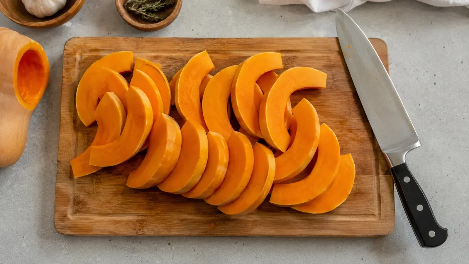 A butternut squash sliced cleanly into even half-moons on a cutting board with a sharp knife resting nearby