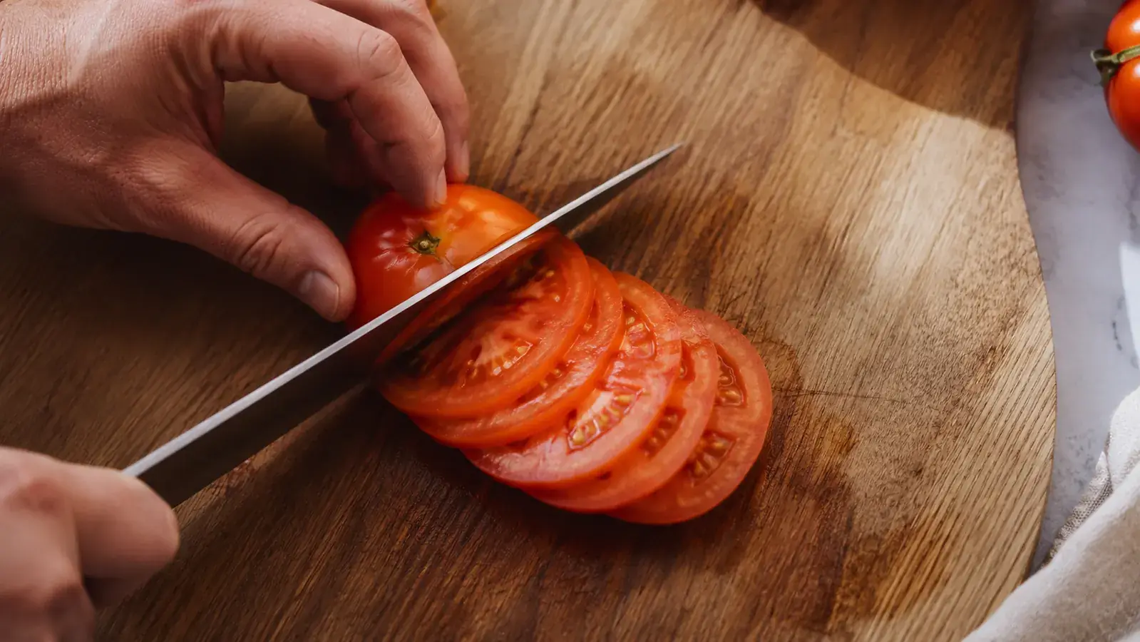Freshly sharpened chef's knife slicing cleanly through a ripe tomato on a wooden cutting board