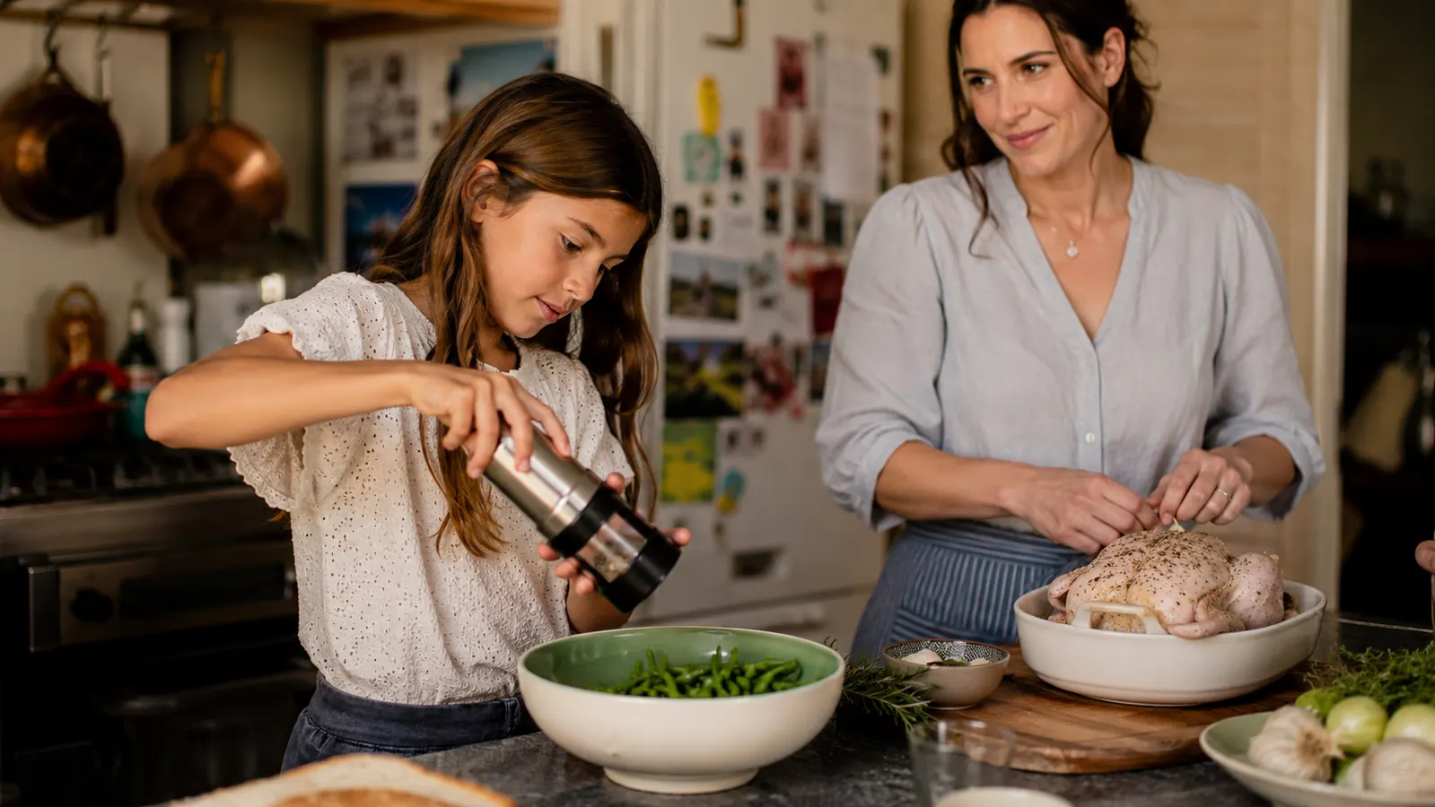 A young girl reaching up to tilt the Circle Joy grinder over a bowl of green beans on a kitchen island
