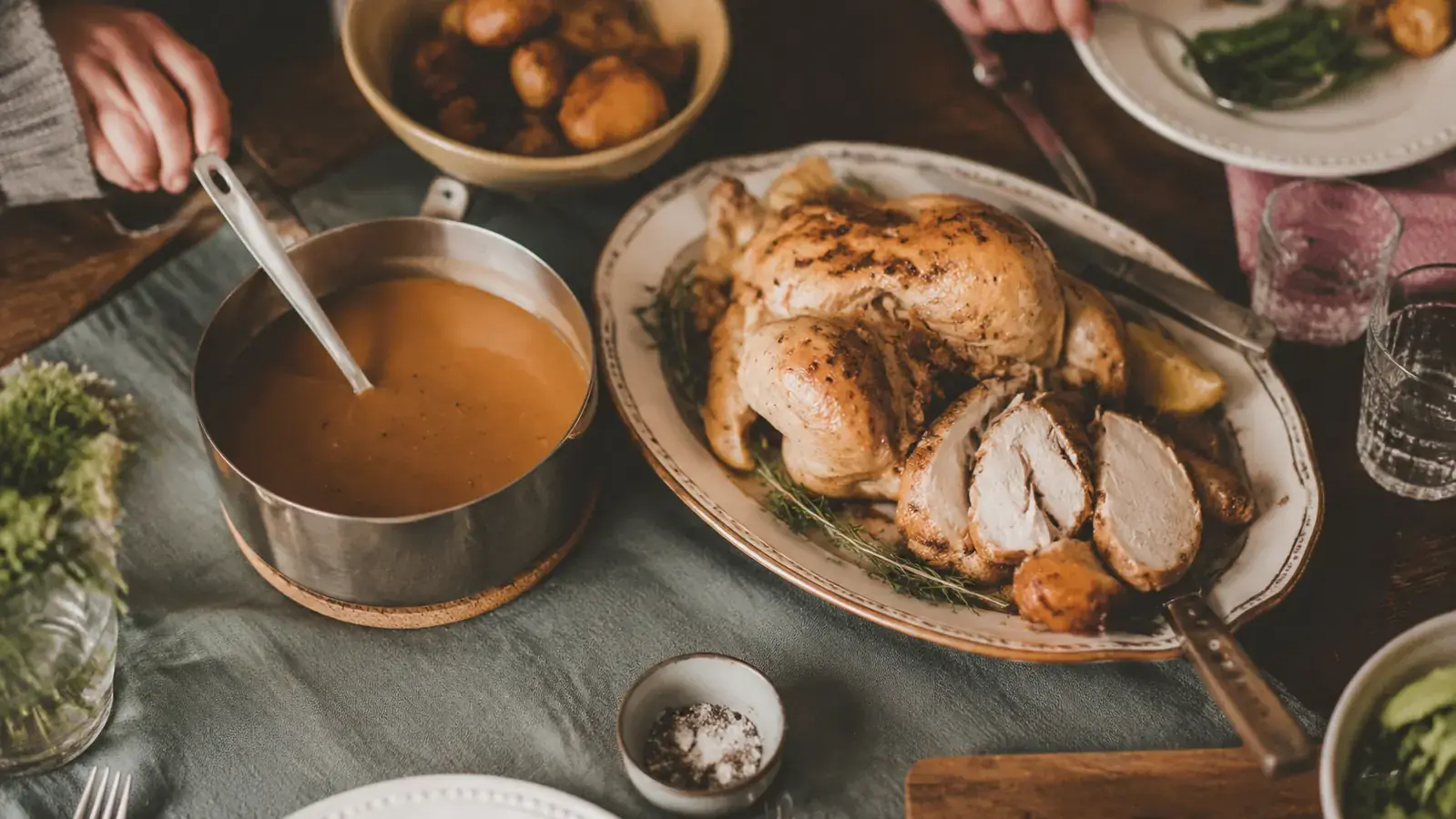 A glossy finished gravy in a saucepan next to a carved roast chicken on a Sunday dinner table