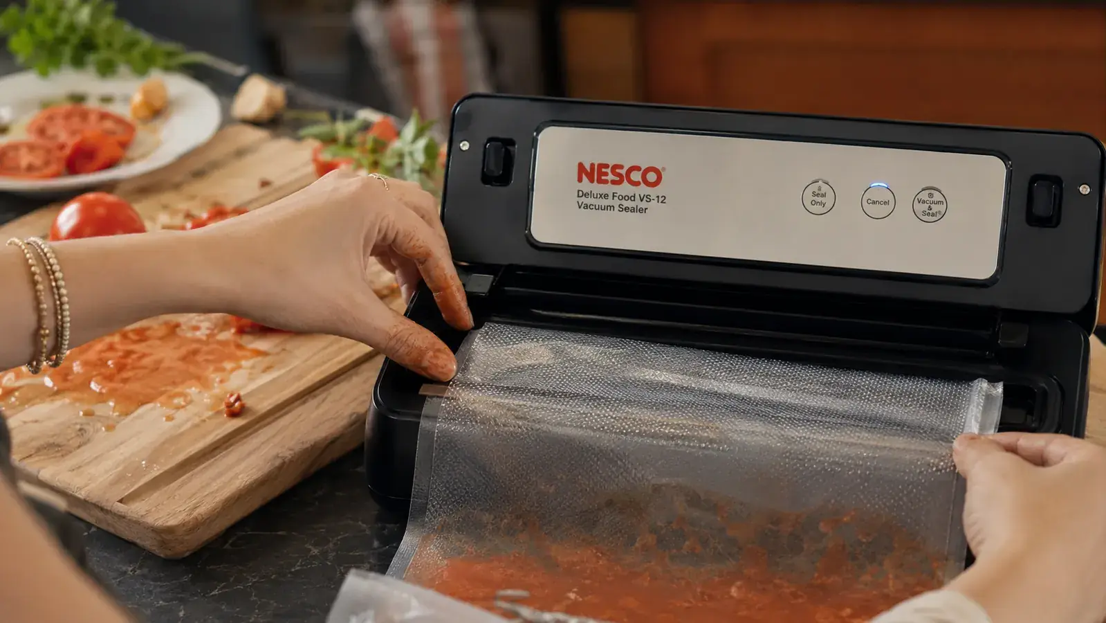 Hand with slightly tomato-stained fingers repositioning a vacuum bag inside the Nesco VS-12's sealing channel