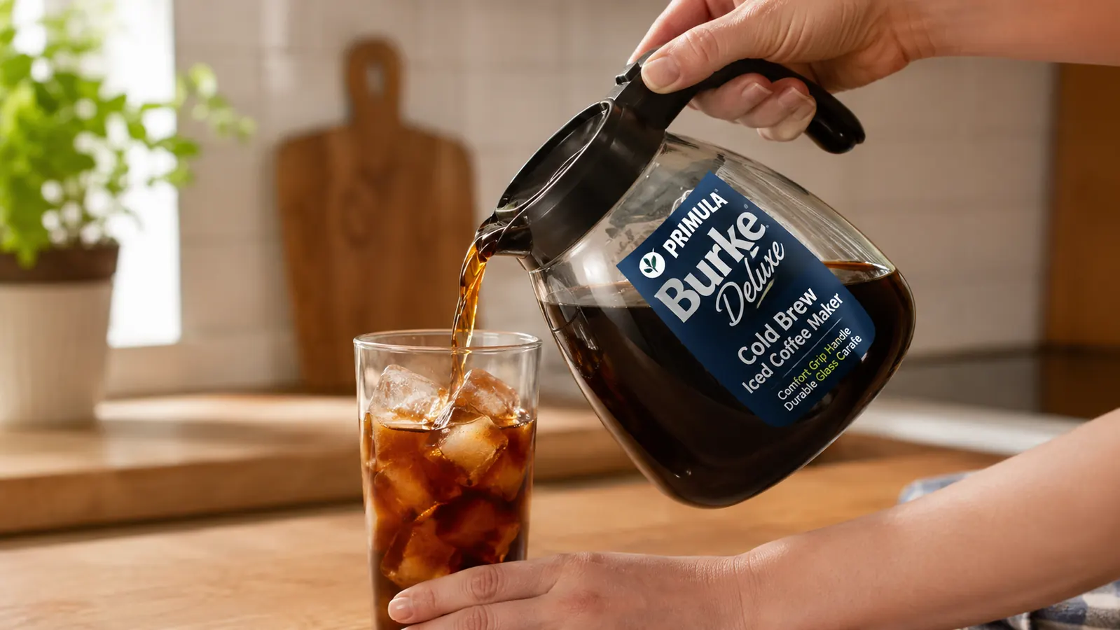 Hand pouring cold brew concentrate from the Primula carafe into a glass of ice