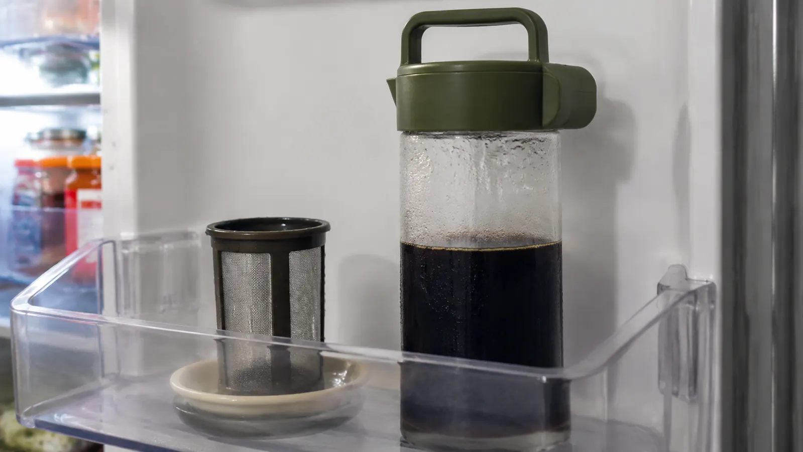 Hario Mizudashi glass pitcher sitting on a refrigerator shelf next to its removable filter basket